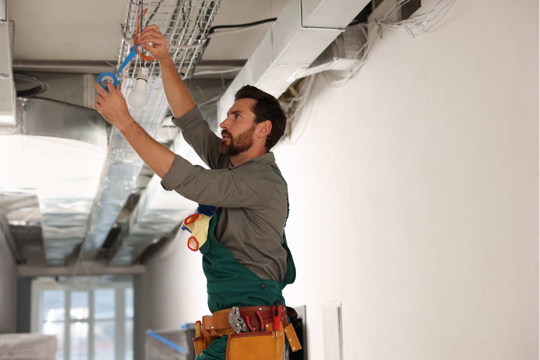 Photo of a male tradesman repairing a light in a building.