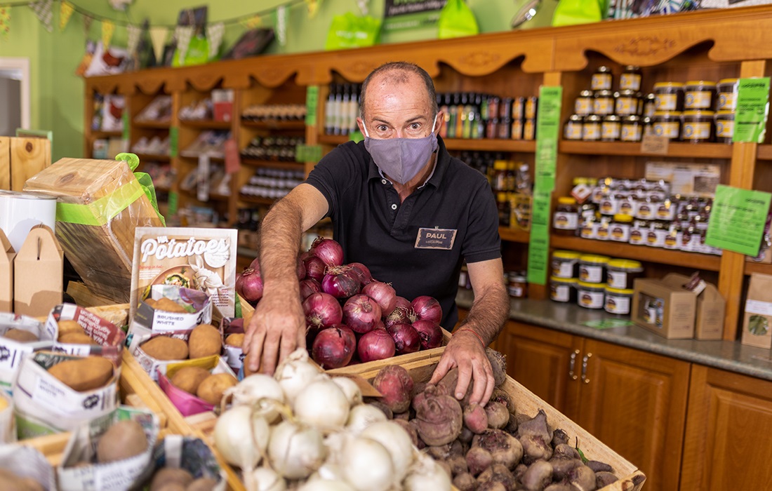 Photo of a grocery store owner. He is managing produce and wearing a mask as part of COVID-19 safety measures.